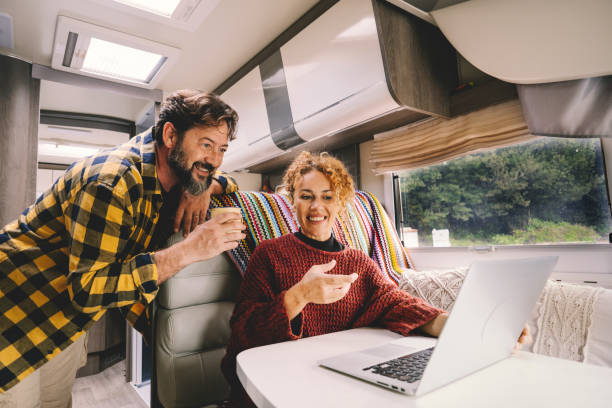 Adult couple enjoy work together using laptop computer sitting inside camper rv vehicle. Concept of nomad and alternative free job lifestyle. Modern man and woman people with technology stock photo