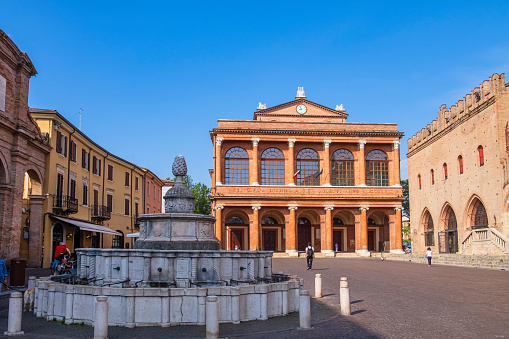 People strolling in Piazza Cavour bordered by ancient buildings, where stands out the Fontana della Pigna, a sixteenth-century fountain ​in white marble.