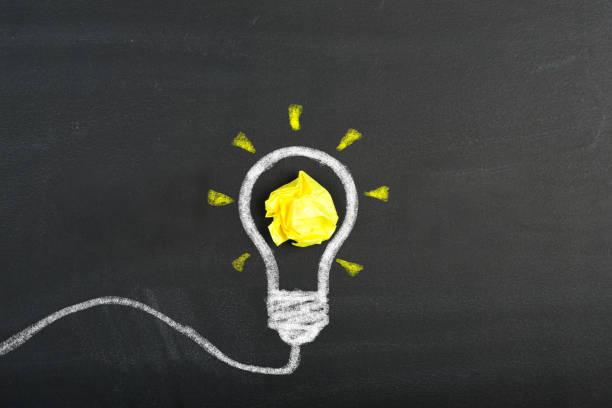 istock Creative thinking ideas and innovation concept. Paper scrap ball yellow color with light bulb symbol on chalkboard 1356748559