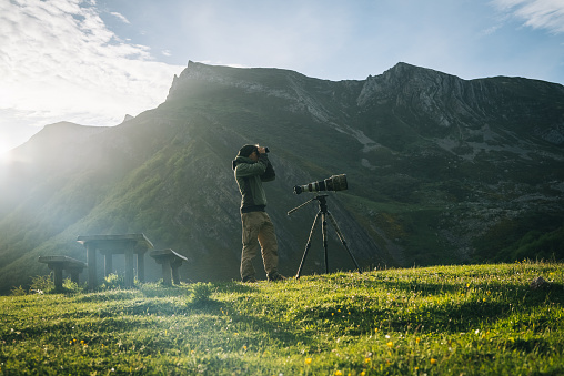 Photographer uses binoculars in a mountain meadow