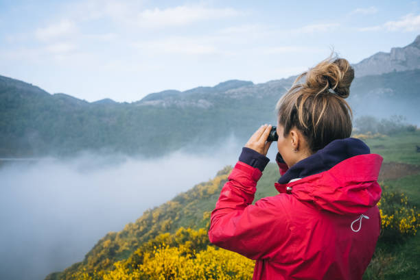 młoda kobieta obserwuje wschód słońca nad górami - binoculars surveillance direction looking at view zdjęcia i obrazy z banku zdjęć