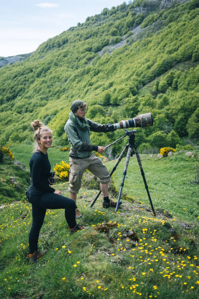 istock Young man and woman with large lens camera on tripod 1356750090