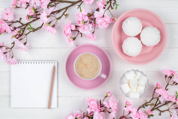 istock Coffee cup with marshmallow in the morning for breakfast. Blank notebook with pen. Diary, planning concept. Romantic spring mockup with copy space. Cherry blossom on white wooden background. Flat lay. 1356755301