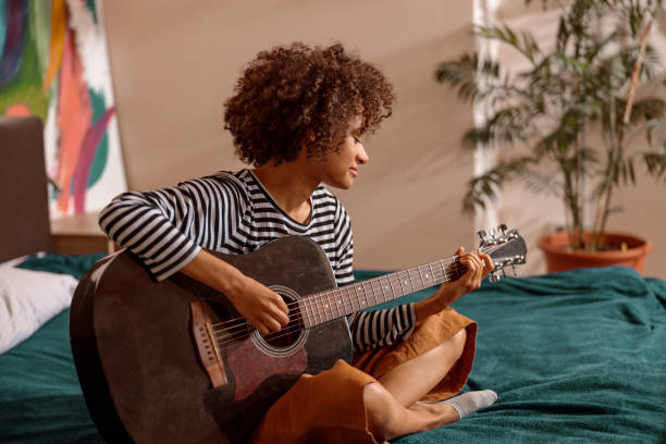 istock Multiracial young woman playing guitar at home 1356757317