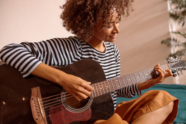 istock Smiling young woman playing guitar at home 1356757338