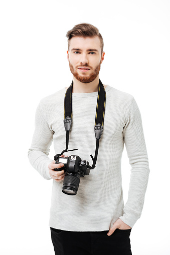 Handsome bearded young man looking at the camera with DSLR camera hanging on the neck isolated