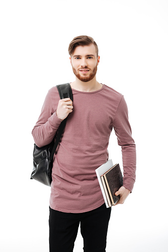 Young handsome male student carrying books and a backpack isolated