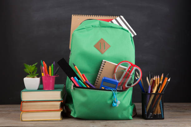 istock Education concept - school backpack with books and other supplies, blackboard background 1356759729