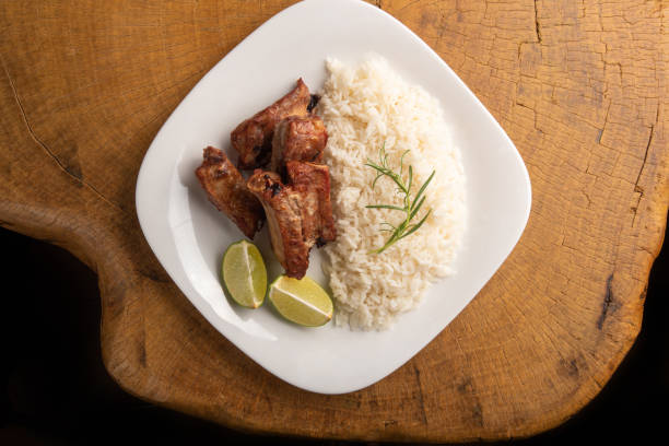 istock Fried pork ribs, rice and condiments on a white plate arranged on light rustic wood, selective focus. 1356760693