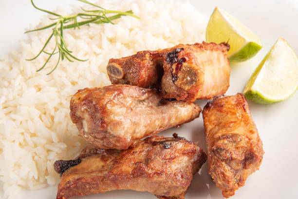 istock Fried pork ribs, rice and condiments on a white plate arranged on light rustic wood, selective focus. 1356761237