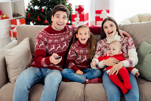 Photo of amazed wife husband children family sit sofa watch tv switch channel xmas spirit indoors inside house home.