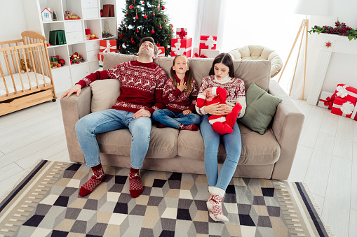 Photo of funny tired husband wife two children wear christmas sweaters sitting sofa sleeping smiling indoors room home house.