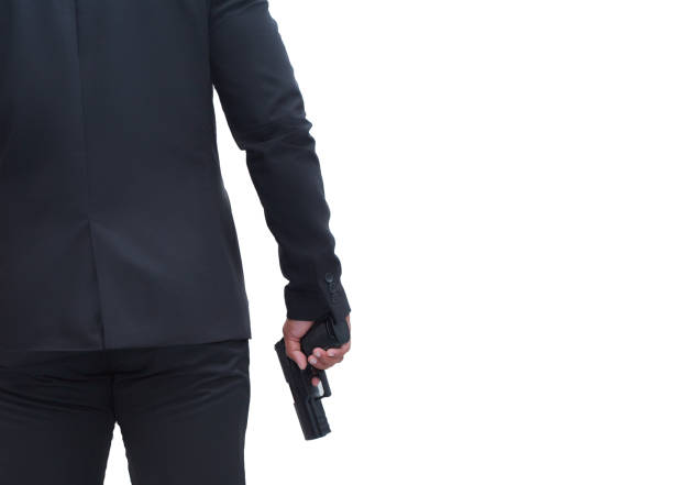 vue arrière d’un homme armé portant un costume noir tenant un pistolet sur fond blanc isolé concept pour assassin, meurtre, criminel, bandit. - gun men spy suit photos et images de collection