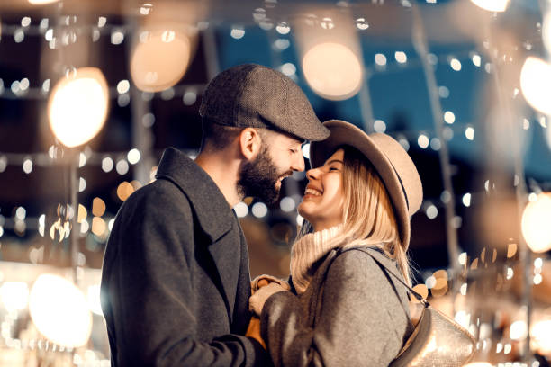 Christmas lovers kissing outdoors on New Year's eve. A young happy couple is standing on the street surrounded by lights and kissing on New Year's eve. stock photo
