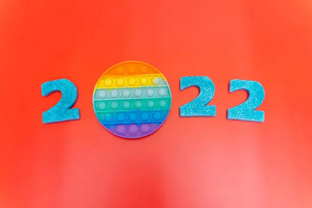 Photo of Numbers 2022 on a red background with a trendy pop it toy. Sparklers are lit on