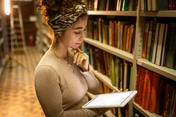 istock Young female student using tablet for reading in the library 1356777699