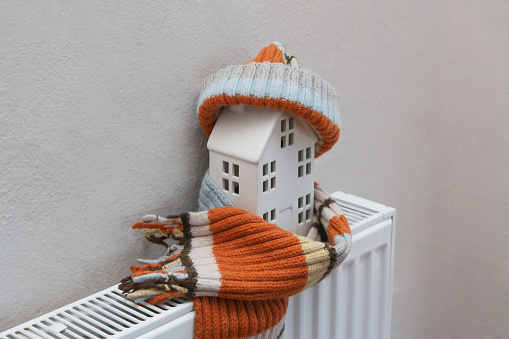 Figure of house and warm clothes on heating radiator. Home heating expenses and savings concept.