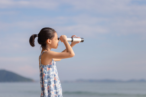 Happy kid playing outdoors on the beach, Asian child girl looking in spyglass