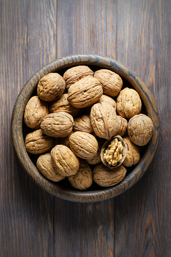 Walnuts in a plate on a brown wooden background. Nuts are a source of vegetable protein. Flat top view.
