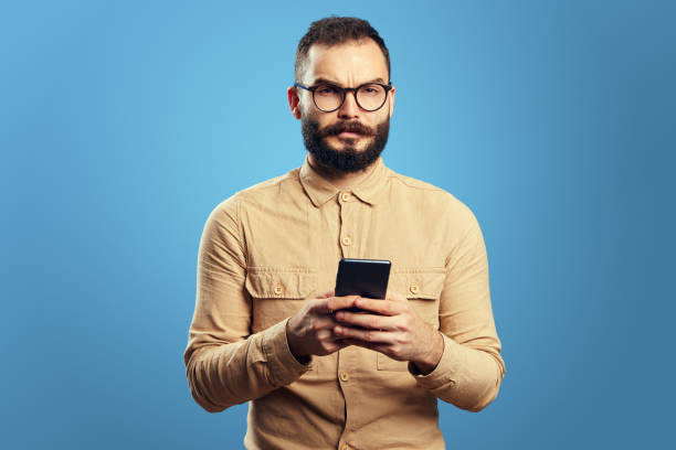 istock Serious adult handsome caucasian man using smartphone on blue background 1356784344
