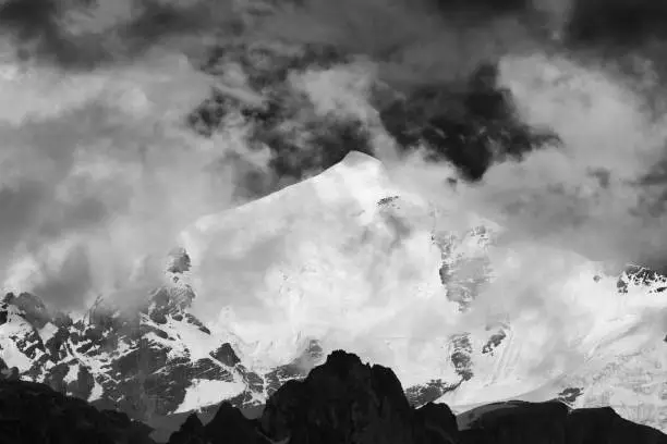Photo of Black and white high snowy mountains with glacier, rocks and sky with dark fog before storm