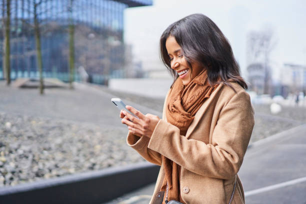 istock Happy woman using mobile phone outdoors in the city during fall wearing coat 1356785371