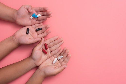 kid's hands with colorful pharmaceutical medicine capsules on pink background