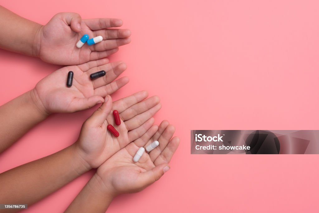 kid's hands with colorful pharmaceutical medicine capsules on pink background Child Stock Photo