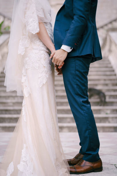 istock Bride and groom stand holding hands on the stone steps. Close-up 1356790702