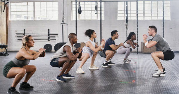 Shot of a group of young people exercising under the watchful eye of their trainer at the gym This will help with posture too! crouching stock pictures, royalty-free photos & images