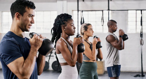 photo d’un groupe de jeunes soulevant des kettlebells ensemble au gymnase - musculation photos et images de collection