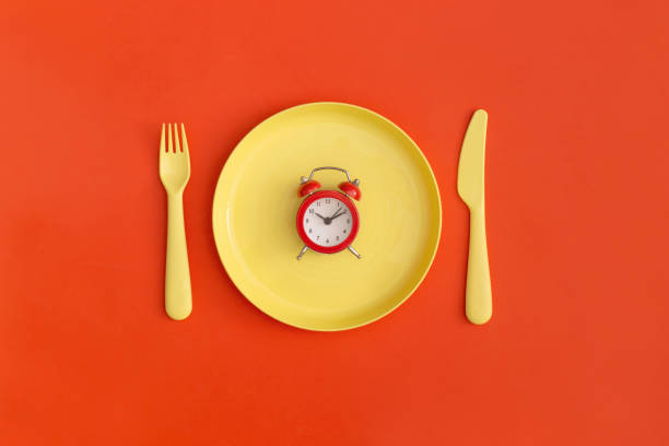 istock Red clock on the yellow plate with fork and spoon on a red background. Top view. Flat lay. 1356792239