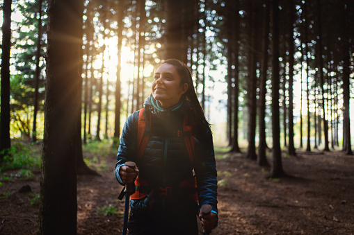 A Caucasian active and healthy woman, in sports clothing hiking with a help of hiking poles in the forest, and admiring the view