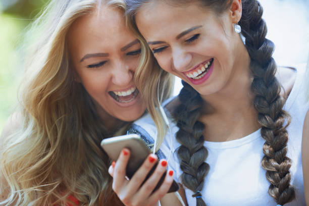 istock Two girlfriends outdoors having fun with smartphone 1356793760