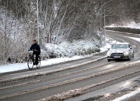 Car driving by a young woman cycling without a helmet on a very slippery bicycle lane. The photo was taken in Holte, a  Copenhagen suburb 2nd of December 2021.