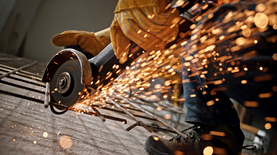 Close-up of construction worker cutting metal grate with angle grinder at site.