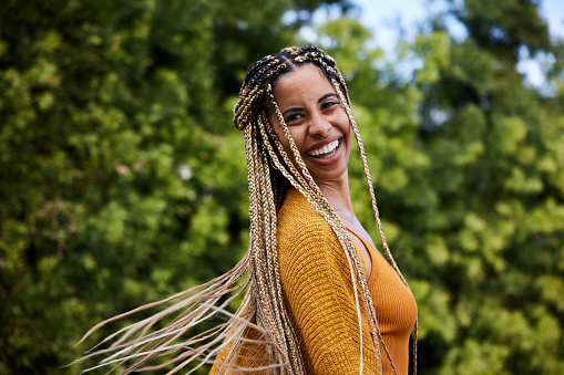 Laughing young woman twirling her long braided hair outside in summer