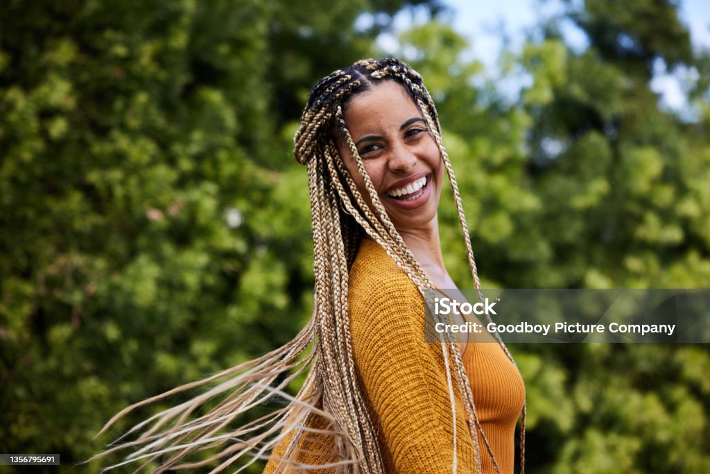 Laughing young woman twirling her long braided hair outside in summer Portrait of a young woman twirling her long braided hair and laughing while standing alone outside in summer Women Stock Photo