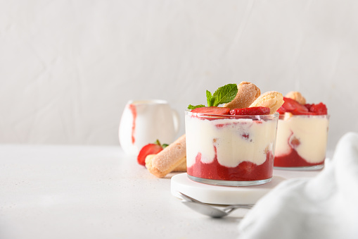 Layered strawberry trifle in glass jars with cookie savoyardi, mascarpone and whipped cream decorated cookie. Close up. Italian tiramisu with berries on white background.