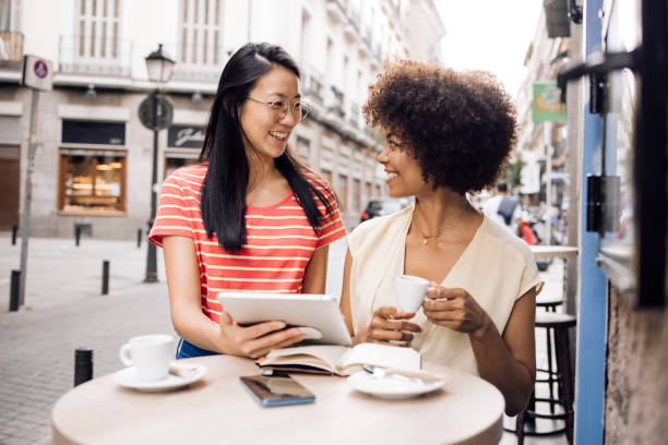 istock Two girls on vacation using tablet at the sidewalk cafe 1356801254