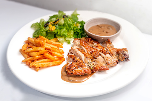 A white dish of chicken breast grilled with french fried and fresh dressing salad