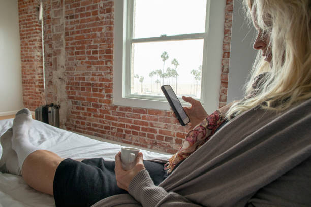Woman reclines on bed and uses smart phone