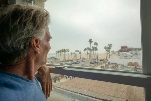reifer mann schaut aus dem fenster zum strand unten - santa monica beach california house stock-fotos und bilder