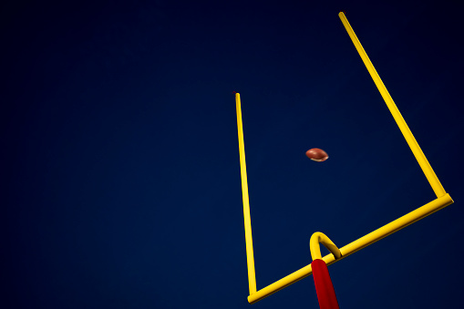 Looking up at yellow football goal post against a dark sky at night as a field goal is made during an American football game.