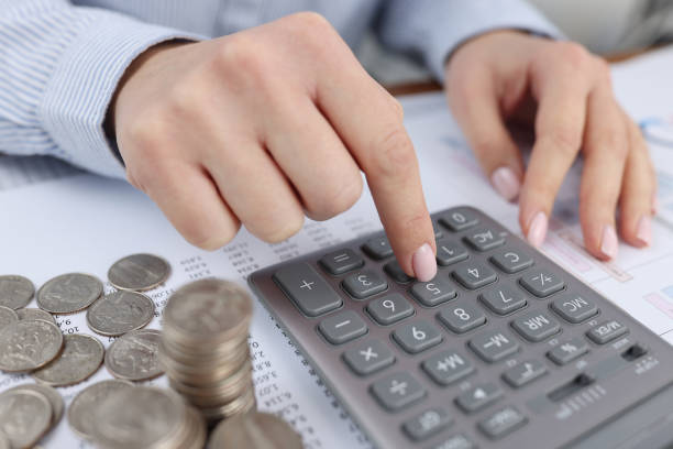 istock Woman counting on calculator at table with documents and coins closeup 1356803319