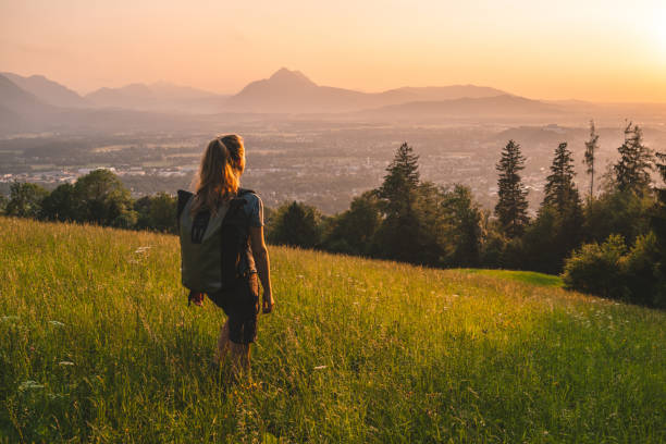 Female hiker relaxes on grassy mountain ridge She looks off to distant European Alps, at sunrise salzburger land stock pictures, royalty-free photos & images