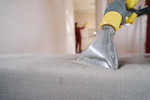 Janitor cleaning upholstered furniture with wet vacuum cleaner