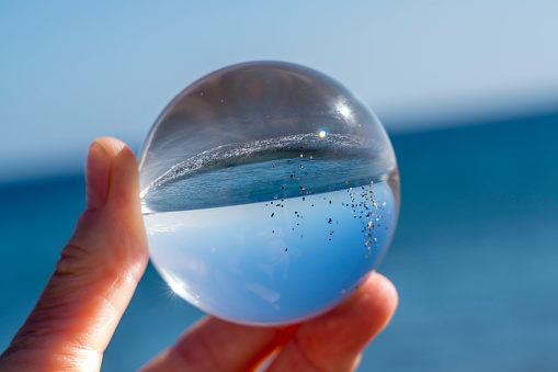 Crystal ball in hand reflecting clear blue sky and sea