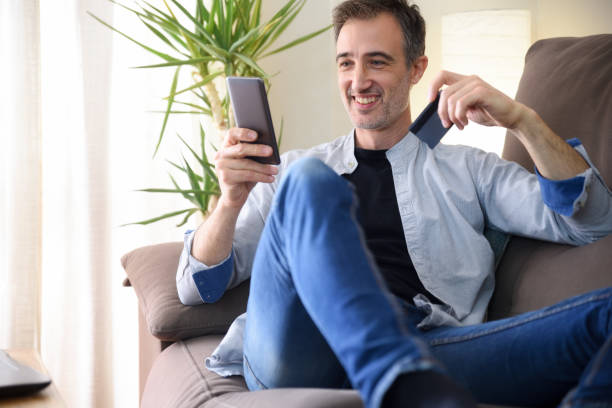 istock Man buying from a smartphone lying on sofa at home 1356810805
