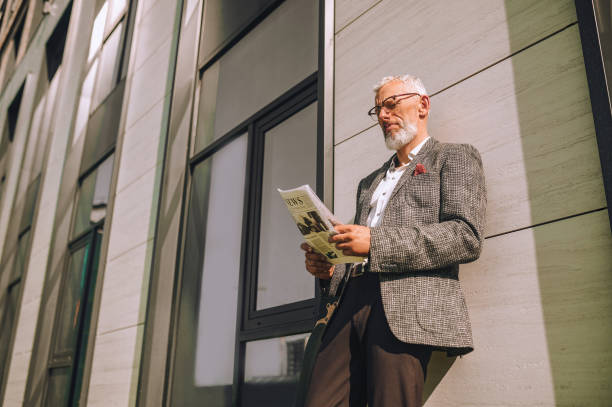 istock A gray-haired businessman reading a newspaper and looking involved 1356812083